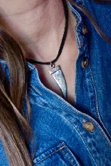 Collar tipo gargantilla con cordón negro y dije de metal plateado en forma de colmillo.
