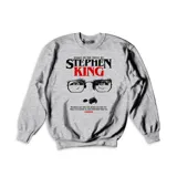 Buzo gris de cuello redondo y manga larga con estampado frontal temático de Stephen King que incluye texto y diseño gráfico.