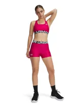 Top deportivo Under Armour de soporte medio, color fucsia con banda elástica inferior negra con el logo de la marca en blanco. Presenta diseño de espalda cruzada y tejido técnico de secado rápido.