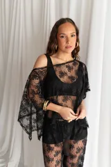 Blusa de tul negro translúcido con aplicaciones de perlas blancas dispersas, de corte amplio y mangas murciélago holgadas.