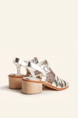 Sandalia plateada de cuero con tiras entrecruzadas, taco de madera y hebilla lateral.