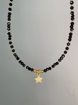 Collar corto con cuentas de cristal facetado negro y pequeñas esferas doradas, con un dije colgante en forma de estrella pavé con circonias.