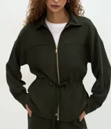 Campera tipo parka color verde oscuro, confeccionada en modal con cierre frontal metálico, cuello camisero, bolsillos frontales y cordón ajustable en la cintura.