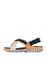 Sandalias Kenner Rakka Cross Craft con tiras cruzadas de tela color beige y ajuste con hebilla de plástico negra. Suela de goma negra con detalles en naranja y verde.