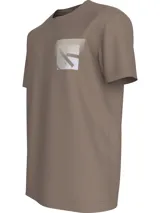 Remera de manga corta color topo (marrón grisáceo) con cuello redondo y bolsillo en el pecho. El bolsillo presenta un estampado difuminado del monograma de Calvin Klein Jeans.