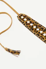Cinturón tipo faja de cuero vacuno con estampado animal print, decorado con tachas metálicas plateadas y tiras laterales con borlas decorativas.