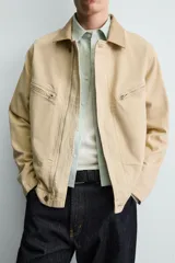 Cazadora relaxed fit de Zara confeccionada en denim de algodón color beige, con cuello de solapa en piel combinada, bolsillos con cremallera en el pecho y cierre frontal oculto.
