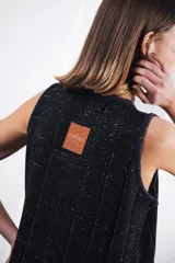 Vestido midi tejido en punto canalé negro con detalles en lurex plateado. Presenta calado artesanal en el ruedo, abertura lateral y etiqueta de cuero en la parte trasera del cuello.