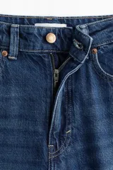 Jean de tiro alto con corte wide leg, confeccionado en denim rígido de lavado azul clásico. Presenta diseño de cinco bolsillos, cierre frontal con botón y ruedo desflecado.