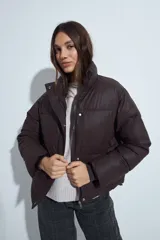 Campera puffer de nylon color marrón oscuro, con cuello alto, cierre frontal y puños elásticos. Diseño acolchado de volumen ligero.