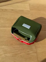 Neceser de neopreno color borgoña, con cierre superior y forro interior. Tiene un asa de mano con una franja azul y blanca.