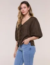 Blusa color beige confeccionada en lino, con escote en V pronunciado y cierre frontal de múltiples lazos para atar. Presenta mangas abullonadas tres cuartos con puños elásticos y corte relajado.