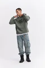 Canguro oversize color verde militar con capucha ajustable, bolsillo frontal tipo canguro y estampa gráfica en el pecho.