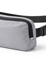 Bandolera color gris con cierre principal y bolsillo frontal con cierre. Cuenta con correa ajustable negra y hebillas de plástico.