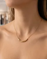 Collar de cadena fina con baño de oro, adornado con una serie de pequeñas esferas y un cubo central.