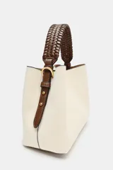 Bolso tipo saca color crudo con cuerpo en tejido canvas, asa corta de mano trenzada en marrón y correa bandolera adicional. Cuenta con cierre de botón imantado y bolsillo interior con cremallera.