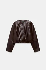 Chaqueta corta de piel color marrón, con cuello redondo, manga larga y cierre frontal con botones. Presenta un diseño con elástico en el ruedo y forro interior.