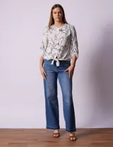 Blusa blanca estampada con flores negras, cuello redondo, abertura con botones y mangas 3/4 con frunce. Tiene terminación con nudo en el ruedo.