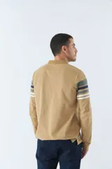 Remera tipo polo de manga larga azul marino con rayas horizontales blancas, grises y rosadas en el pecho. Tiene cuello clásico con botones y logo estampado en el pecho. Corte regular.