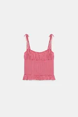 Top de escote redondo y tirantes finos con lazada, con estampado de cuadros vichy en rojo y blanco. Presenta frunces en el pecho y detalle de volados en el ruedo.