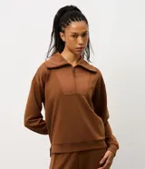 Buzo deportivo de corte oversized en color verde oliva, confeccionado en tejido modal con mezcla de poliéster y elastano. Presenta cuello alto con cierre frontal de cremallera y paneles frontales con textura acanalada. Incluye mangas largas con puños elásticos ajustados.