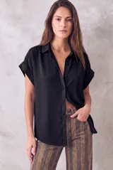 Blusa negra de manga corta, cuello camisero y cierre frontal de botones, con diseño holgado y fluido.