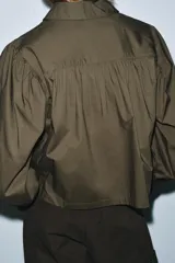 Camisa de popelín color blanco con cuello solapa, cierre frontal con botones ocultos y mangas largas abullonadas con puños estructurados.