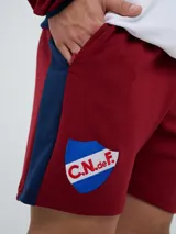 Bermuda deportiva Umbro del Club Nacional de Football, color azul marino, con cordón ajustable en la cintura, bolsillos laterales, el escudo del club en una pierna y el logo de la marca en la otra.