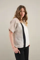 Blusa de lino de diseño contemporáneo, con escote cuadrado y mangas cortas en recortes que combinan distintas texturas. Su propuesta incorpora una franja vertical en contraste que aporta dinamismo y personalidad, mientras que el calce relajado la convierte en una prenda fresca y versátil.
