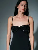 Vestido largo negro de corte recto con breteles finos. Presenta un detalle de frunce en el busto con aplicación de lentejuelas y un tajo lateral en la falda.