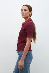 Camisa de manga corta en color bordó, confeccionada en tejido con textura de punto smock. Presenta cuello clásico, cierre frontal con botones y un ajuste entallado al cuerpo.