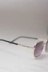 Lentes de sol rectangulares con marco dorado y lentes degradadas de violeta a transparente.