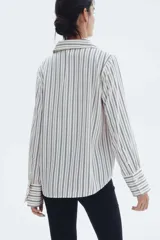 Blusa de manga larga a rayas verticales blancas y negras, con cuello clásico, escote en V y cierre frontal con botones. Puños con detalle de rayas horizontales y bajo redondeado.