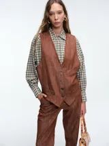 Chaleco estructurado de denim color terracota, con escote en V, cierre frontal con botones y bolsillos laterales tipo ojal.