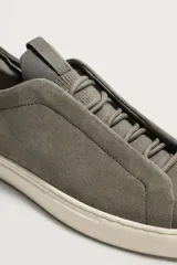 Zapatilla de piel con acabado en serraje de color gris, diseño de cordones ocultos y suela de goma en contraste de color blanco.