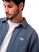 Camisa de manga larga confeccionada en tejido tipo waffle, color azul grisáceo. Presenta cuello clásico, cierre frontal con botones y un bolsillo en el pecho con etiqueta de la marca.