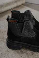 Bota tipo chelsea de punta redonda, confeccionada en una combinación de cuero texturizado y gamuza en tonos marrones. Presenta elásticos laterales negros y una suela track robusta de goma negra.