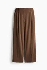 Pantalón de corte holgado color marrón, de estilo sastrero, con cintura clásica, trabillas para cinto y cierre con botón y cremallera. Presenta piernas rectas con pinzas frontales y bolsillos laterales.