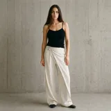 Pantalón de corte ancho, color beige con rayas diplomáticas finas y diseño cruzado envolvente en la parte delantera, con cierre lateral mediante hebilla ajustable.