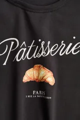Remera corta de algodón color gris oscuro, con cuello redondo, mangas cortas y estampa frontal con la frase "Pâtisserie Paris" y un dibujo de un croissant.