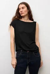 Blusa blanca de manga corta y corte recto, con escote bote y detalle metálico circular en el hombro.