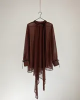 Camisa de gasa color marrón oscuro, de corte oversize y cuello alto fruncido con cordones colgantes. Presenta mangas largas abullonadas con puños ajustados por lazos y dobladillo asimétrico con terminación en puntas.