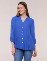 Blusa azul de silueta suelta y textura liviana, con escote en V y cuello mao. Cuenta con acceso frontal mediante abotonadura completa, alforzas verticales en el pecho, y mangas tres cuartos con galón calado tipo puntilla y puños elastizados.