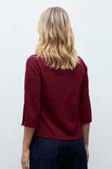 Sweatshirt color bordó con cuello redondo y mangas tres cuartos. Presenta detalles de botones metálicos decorativos a lo largo de los hombros y las mangas.