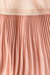 Vestido corto de corte holgado en crepé rosado claro, con escote en V pronunciado adelante y atrás, y breteles finos que se entrelazan en la espalda. Presenta un volado plisado en el borde inferior en un tono rosado más oscuro.