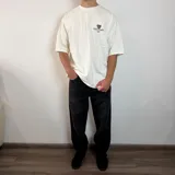 Remera negra de corte oversize con estampa gráfica en la espalda que presenta un oso con anteojos y bandana, acompañada de la frase 'Richer, Louder & Unbothered Than Ever'.