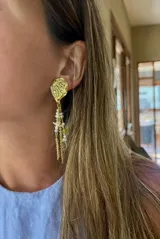 Aros colgantes dorados con base irregular y dijes de cadena dorada, perlas y piedras de colores.