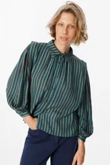 Camisa de manga larga con diseño de rayas verticales en tonos verde, azul y marrón. Presenta cuello clásico, cierre frontal con botones y mangas abullonadas con puños ajustados.