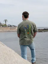 Remera Brixton oversize de algodón, color marrón con efecto acid wash, manga corta y estampa en la espalda de flores de mburucuyá con el texto vertical en color verde.