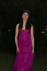 Vestido largo fucsia con corte bajo el busto, escote en V y top de triángulos con detalles dorados. Presenta cut outs en la cintura, breteles finos cruzados en la espalda, corte en la cadera y falda larga con tajo y volados.